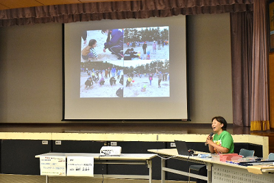 スクリーンを見せながら話す女性の写真