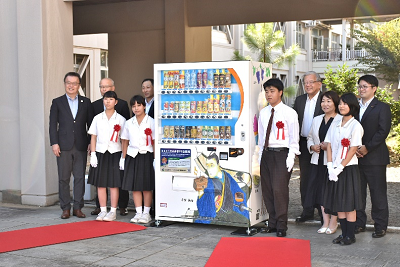 赤いバラと紅白のリボンを胸に付けた人たちが自動販売機の周りに並んでいる写真