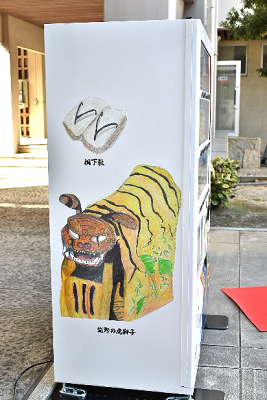 自動販売機の側面に桐下駄や虎獅子のイラストが描かれている写真