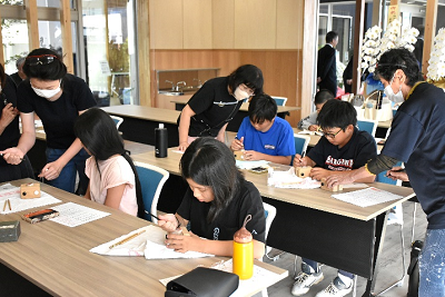 彫刻刀で作業する子供たちと見守る大人たちの写真