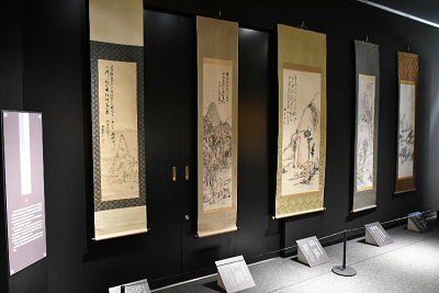 黒い壁面に山水画などの掛け軸が並べて展示されている写真