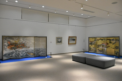 白い壁の広い空間で屏風や絵画が飾られている写真