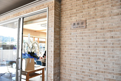 レンガ調の外壁に「談話室」のプレートが掛かり、ガラス戸の奥にテーブルと花が飾られた室内が見える写真