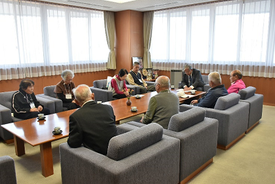 高齢の男女が並べられた椅子に座って話している写真