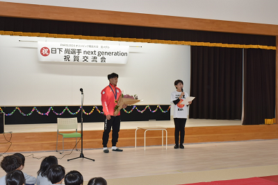 花束を持ったジャージ姿の人の隣で話す女性の写真