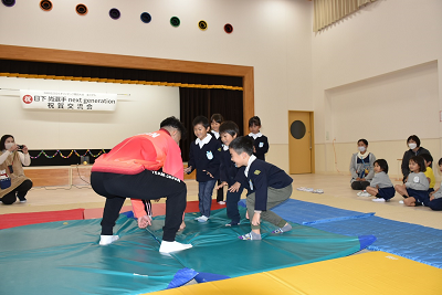 園児たちと相撲をするジャージ姿の人の写真