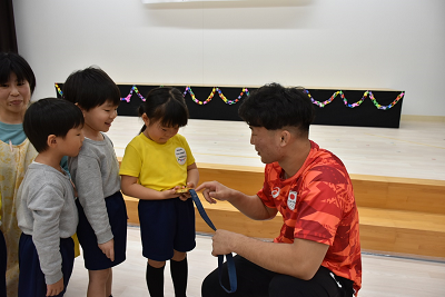 金メダルを園児たちに見せるジャージ姿の人の写真