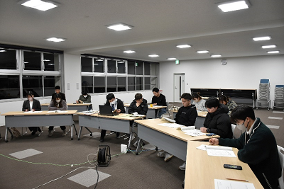 机に座って手元の資料を見ている人達の写真