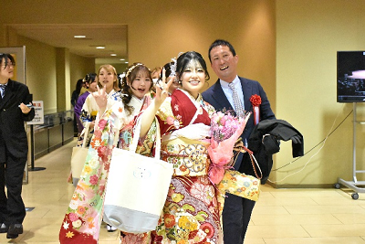 赤い振り袖姿の女性が片手に花束を持ち、もう片方の手でピースサインしている写真