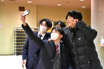 スーツを着た男性たちがスマートフォンで自撮りしている写真