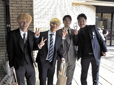 スーツを着た男性4人が並んでピースサインしている写真