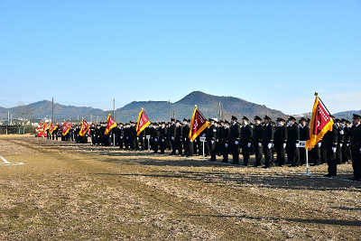 山脈の見える広場で整列する消防団制服姿の人たちの写真