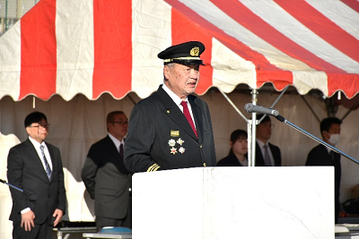 胸元に複数のバッジがついた消防団制服を着た男性が演台で話している写真