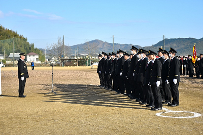2列に並んで起立する消防団制服を着た人たちと向かい合って立つ男性1人の写真