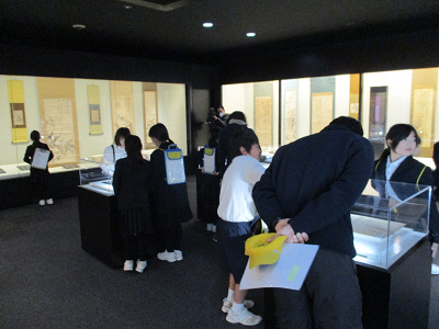 照明が控えめの部屋で児童たちが展示物を見ている写真