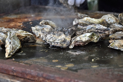 鉄板で焼かれた殻付き牡蠣が湯気を立てている写真