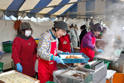 赤いエプロンに青い手袋をした2人の女性が調理を行っている写真
