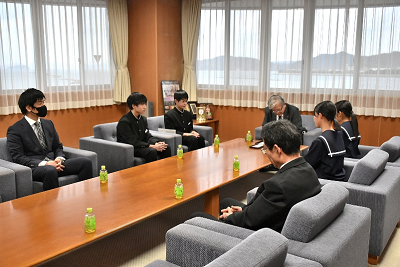 椅子に座っているスーツ姿の男性と話す生徒たちの写真