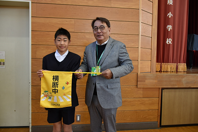 制服姿の児童とスーツ姿の男性が横断旗を持っている写真
