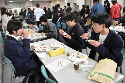 たくさんの人の中でご飯を食べる男性3人の写真
