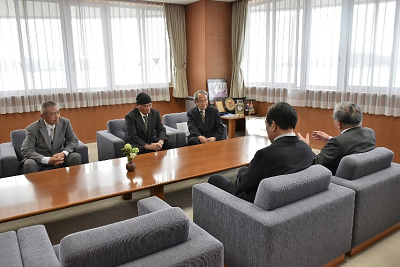 応接室で、長いテーブルを挟んで5人の男性が向かい合って座り、手前の男性が話している写真