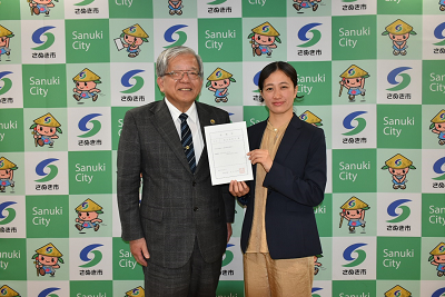 委嘱状を持った女性と男性の記念写真