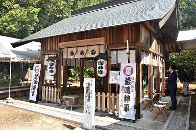 釜鳴神事の看板が立てられた三角屋根の建物の写真