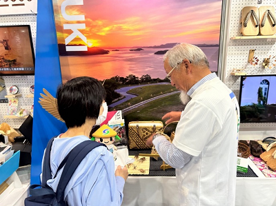 机の上に置かれた展示物の前で男性が女性へ説明をしている写真