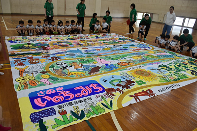 「さぬきいのちのみち」が書かれた巨大な絵の周りに体育座りしている園児達の写真
