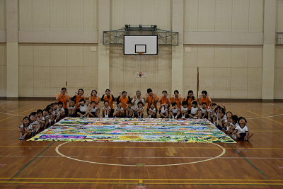 バスケットゴールの下に置かれた巨大な絵の周りに園児たちが集まっている写真