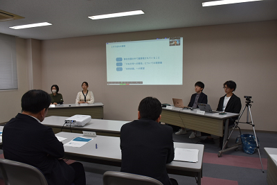 スクリーンを使用した説明を受けているスーツ姿の人たちの写真