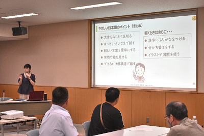 スクリーンを見せながら話す女性の写真