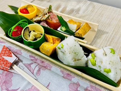 竹の皿に並んだ枝豆おにぎりとおかずの写真