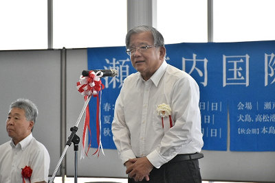 紅白リボンのついたマイクの前に立つ男性の写真