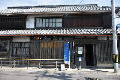 瓦屋根で二階建ての木造建築の前に青いのぼりが置かれている写真