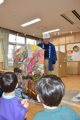 凧を見せる男性と凧を見る園児たちの写真