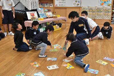 かるたで札を取り合う生徒と園児2人