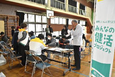 テーブル越しで椅子に座り、血圧や骨密度などを測定する測定者と参加者