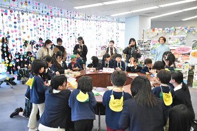 円になって一緒に折り紙のアサガオを作る生徒と園児