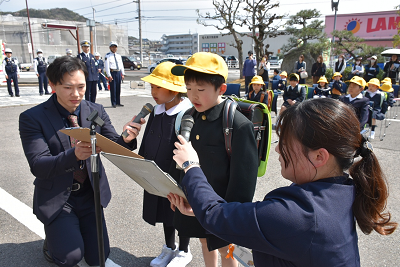 交通安全誓いの言葉を宣誓する男子児童と女子児童とそれぞれにマイクを向ける男性と女性