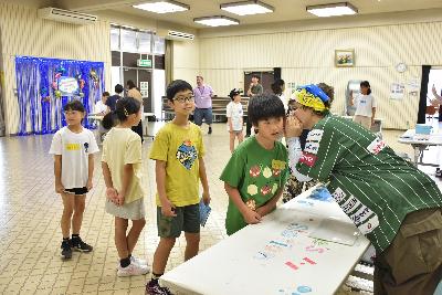 伝言ゲームで、ALTが初めの男の子にフレーズを伝える様子
