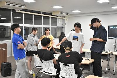 机を囲む複数の男女が話し合う様子