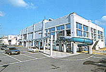 駐車場に隣接して建っている白い外装の建物の写真