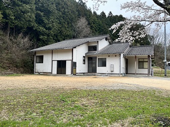 桜の木がある広い庭に建つ白い壁の「さぬき市移住体験ハウス（多和）」の外観写真