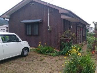 敷地内に軽自動車が停まっている茶色い外壁の「さぬき市移住体験ハウス（津田）」の外観写真