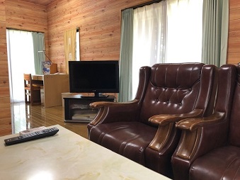 茶色い革張りのソファとテレビが置かれた木目調の壁のリビングルームの写真