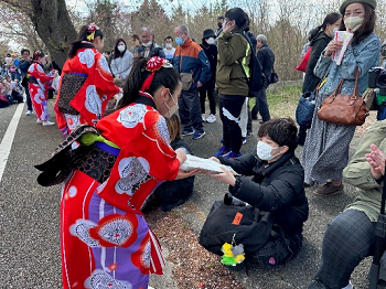 祭り衣装を着た「さぬき舞人」の女性が座っている男性客に配布物を渡している写真