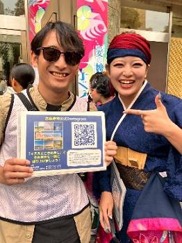 金沢をアピールするボードを持った男性と祭り衣装に身を包んだ「さぬき舞人」の女性が笑顔で並んでいる写真