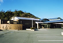 舗装された駐車場の奥に丸い屋根の平屋の建物の写真